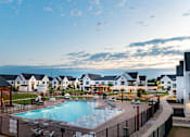 Thumbnail 23 of 38 - A large outdoor swimming pool surrounded by a fence and a wooden pergola.