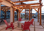 Thumbnail 25 of 30 - A wooden pergola with red chairs and a table is set up outside.