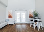 Thumbnail 15 of 29 - A white couch with a blue pillow is in front of a painting in a room with a wooden floor.