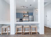 Thumbnail 12 of 29 - A kitchen with white walls and a white counter top with three stools.
