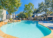 Thumbnail 50 of 62 - A large outdoor swimming pool surrounded by trees and a stone wall.