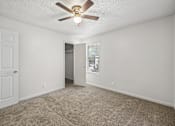 Thumbnail 6 of 23 - A room with a ceiling fan and carpeted floor.