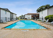 Thumbnail 12 of 23 - A swimming pool surrounded by chairs and apartment buildings.