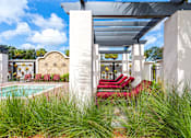 Thumbnail 33 of 40 - A white building with a pool and red chairs.