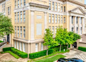 Thumbnail 12 of 13 - A large, beige building with a classical design and a green lawn in front.