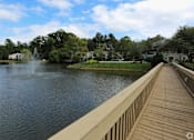 Thumbnail 16 of 16 - A wooden walkway leads to a fountain in the middle of a lake.
