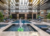 Thumbnail 10 of 30 - a pool with a fountain and lounge chairs in front of an apartment building