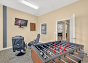 Thumbnail 14 of 20 - A foosball table is in the middle of a room with a television mounted on the wall.