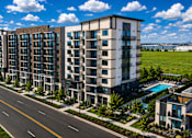 Thumbnail 26 of 26 - A modern apartment building with a pool and a road in front.