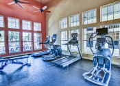 Thumbnail 14 of 26 - A gym with treadmills, elliptical machines, and a fan.