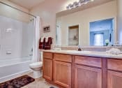 Thumbnail 13 of 26 - A bathroom with a wooden vanity and a white bathtub.