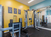 Thumbnail 22 of 40 - A gym with a yellow wall and a variety of equipment.