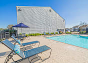 Thumbnail 34 of 40 - A pool area with lounge chairs and umbrellas in front of a building.