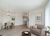 Thumbnail 3 of 19 - A living room with a grey couch, a brown coffee table, and a dining table with chairs.