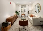 Thumbnail 3 of 21 - A living room with a brown chair, a white couch, and a round mirror on the wall.