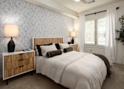 Thumbnail 4 of 21 - A bedroom with a large bed, a nightstand with a lamp, and a potted plant.