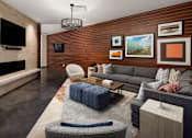 Thumbnail 11 of 21 - A living room with a grey couch, a blue ottoman, and a fireplace.