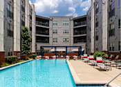 Thumbnail 14 of 21 - A swimming pool in front of a building with red lounge chairs.