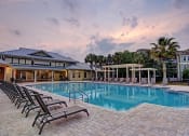 Thumbnail 1 of 26 - A large swimming pool surrounded by lounge chairs and a building in the background.