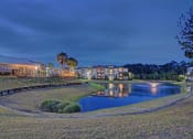 Thumbnail 21 of 26 - A serene landscape with a lake, a bridge, and a building with lights on.