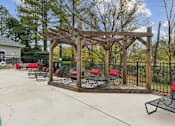Thumbnail 29 of 45 - A wooden pergola with red cushioned chairs and a black metal fence.