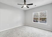 Thumbnail 39 of 45 - A room with a ceiling fan and a window showing a parking lot outside.