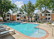 Thumbnail 30 of 38 - A swimming pool surrounded by lounge chairs and trees in front of apartment buildings.