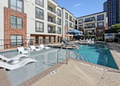 Thumbnail 4 of 26 - A pool with a slide and sun loungers in front of apartment buildings.
