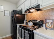 Thumbnail 11 of 29 - A kitchen with a black refrigerator and stove top oven.