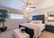 Thumbnail 16 of 29 - A bedroom with a large bed, a ceiling fan, and a potted plant.