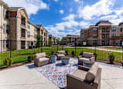 Thumbnail 19 of 32 - A patio with a rug and chairs in front of apartment buildings.