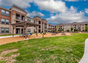 Thumbnail 28 of 32 - A large grassy area in front of apartment buildings with picnic tables.