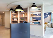 Thumbnail 24 of 27 - A modern interior with a black reception desk and a shelf with decorative items.