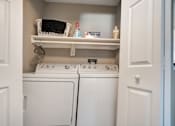 Thumbnail 28 of 35 - A white laundry room with two washing machines and a shelf above them.