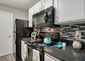 Thumbnail 17 of 35 - A black refrigerator and microwave in a kitchen with a white door.
