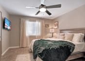 Thumbnail 22 of 35 - A bedroom with a bed, a ceiling fan, and a television mounted on the wall.
