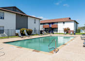 Thumbnail 11 of 14 - A swimming pool surrounded by lounge chairs and a building in the background.