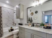 Thumbnail 21 of 24 - A bathroom with a marble tub surround and a large mirror above the sink.