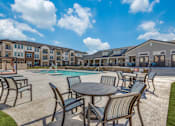Thumbnail 9 of 24 - A sunny day at the outdoor pool area of a resort with chairs and tables arranged around the pool.