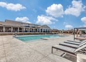 Thumbnail 8 of 24 - A swimming pool with sun loungers and a building in the background.