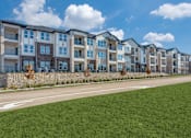 Thumbnail 4 of 24 - A row of modern apartment buildings with a grassy area in front.