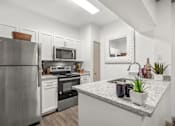 Thumbnail 11 of 43 - A modern kitchen with a stainless steel refrigerator, microwave, oven, and sink.