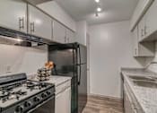 Thumbnail 11 of 22 - A kitchen with a black refrigerator, white cabinets, and a black gas stove.