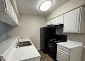 Thumbnail 3 of 10 - A small kitchen with a black refrigerator and white cabinets.