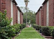 Thumbnail 1 of 10 - A long row of red brick buildings with green bushes in front.