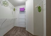 Thumbnail 6 of 28 - A walk-in closet with white shelves and a carpeted floor.