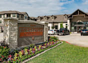 Thumbnail 1 of 28 - The image shows the entrance to West Creek Apartments with a sign and a flower bed in the foreground.