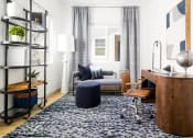 Thumbnail 27 of 30 - a living room with a blue rug and a desk with a chair and a couch in the