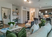 Thumbnail 2 of 33 - a living room with a couch and a coffee table in front of a kitchen with a counter