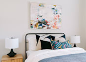Thumbnail 5 of 22 - A bed with a white comforter and a blue blanket with a white pillow and a painting on the wall.